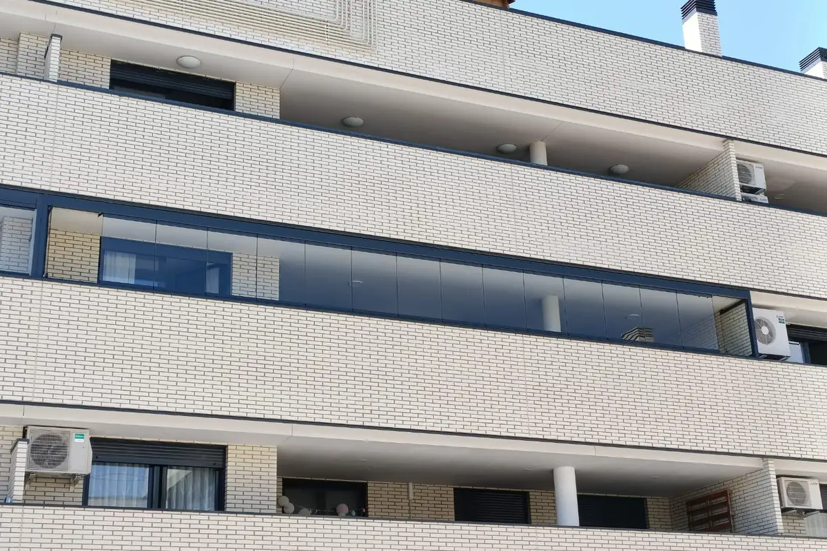 Fachada de edificio con un balcón cerrado con cortina de cristal corredera