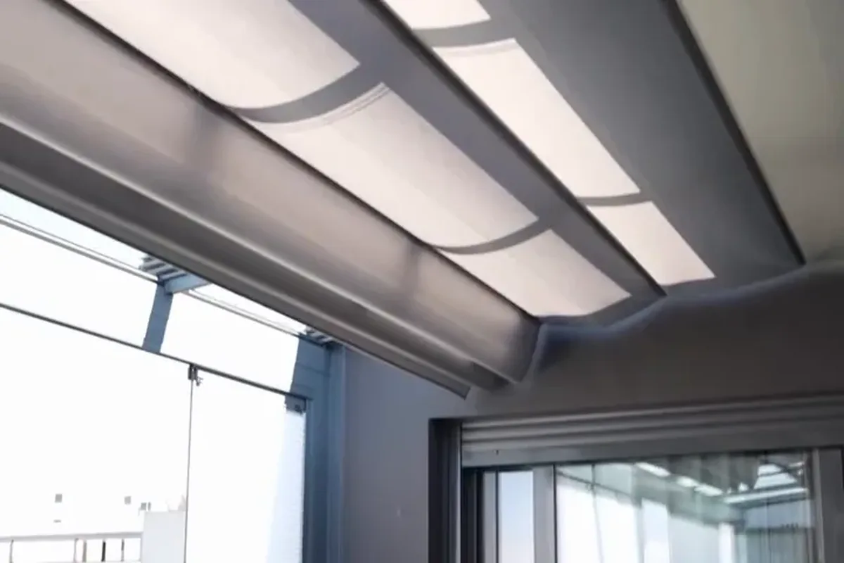 Techo de cristal visto desde dentro de una terraza cerrada, con un toldo de tela bajo el vidrio y perfilería de aluminio gris