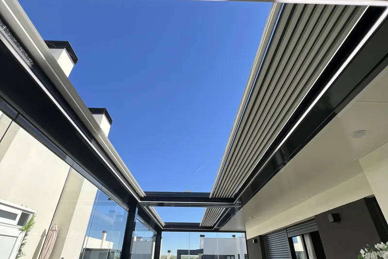 Terraza cubierta con pérgola bioclimática de lamas y cerramiento de cristal, sofá y vistas a jardín