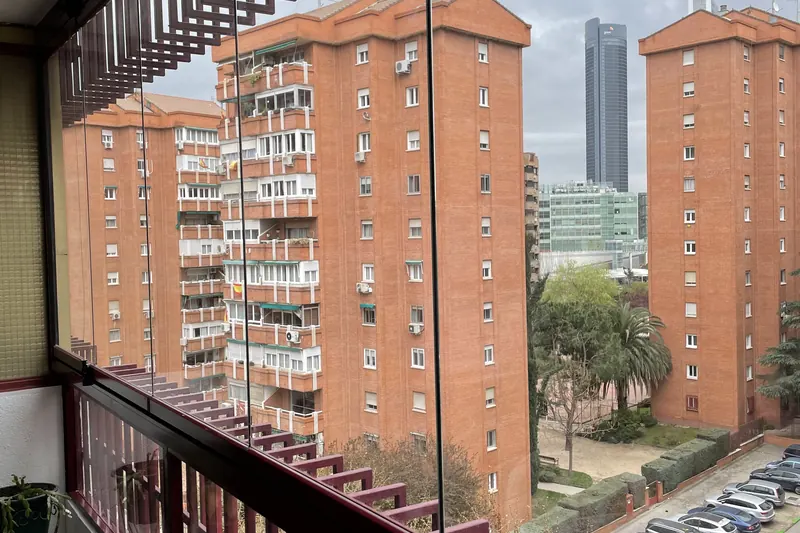 Cortina de cristal en balcón con barandilla decorativa y vistas al skyline de Madrid