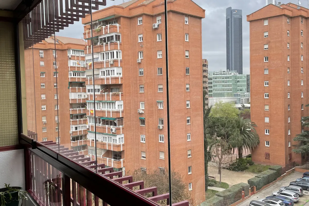 Cortina de cristal en balcón con barandilla decorativa y vistas al skyline de Madrid
