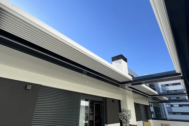 Terraza cubierta por pérgola bioclimática con mesa auxiliar y sillas junto a la fachada