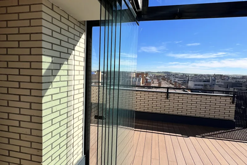 Cortina de cristal abatible en esquina de ático junto a una chimenea