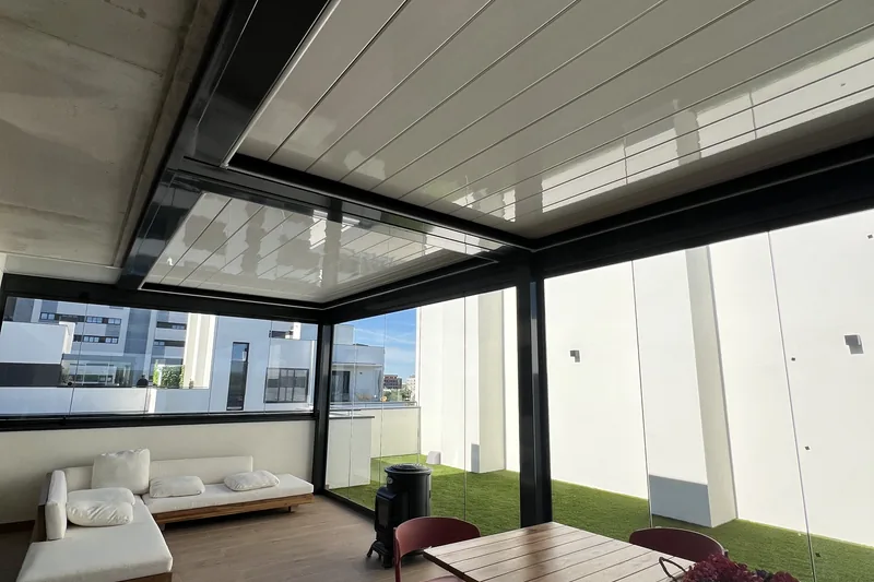 Pérgola bioclimática con lamas cerradas sobre terraza con comedor, sofá y cerramiento de cristal