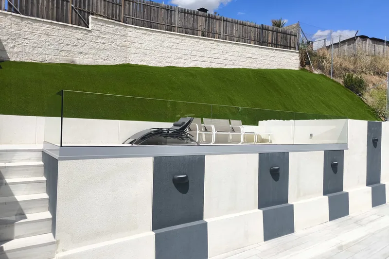 Barandilla de cristal laminado sin postes en terraza elevada junto a césped artificial