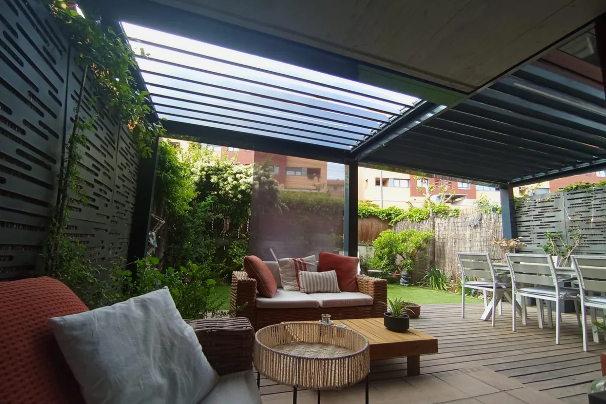 Salón exterior bajo pérgola bioclimática con sofas de fibra sintetica junto a jardín