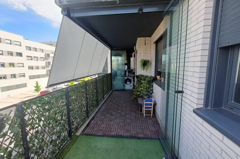 Toldo veranda gris sobre un balcón con césped artificial y valla de hiedra