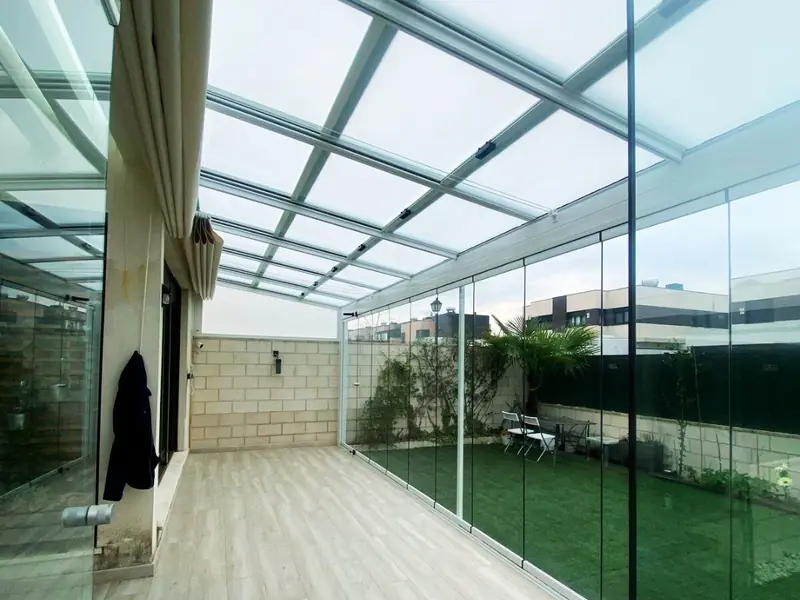 Interior de un porche acristalado con las cortinas de cristal abatibles abiertas y el techo de cristal encima, en Madrid