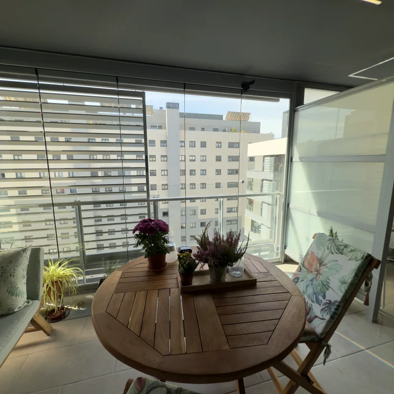 Balcón cerrado con cortina de cristal corredera y mesa de exterior en vivienda de Madrid
