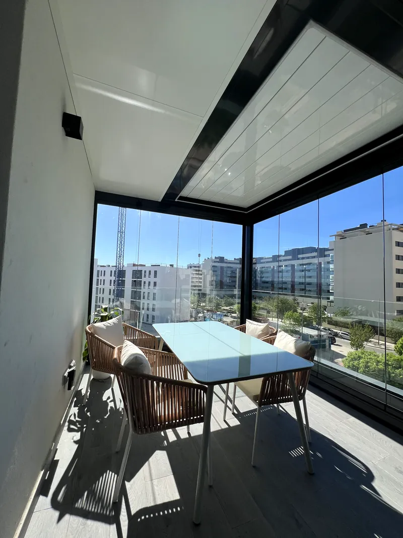 Cerramiento de cristal en esquina con mesa de comedor y vistas a edificios de la ciudad