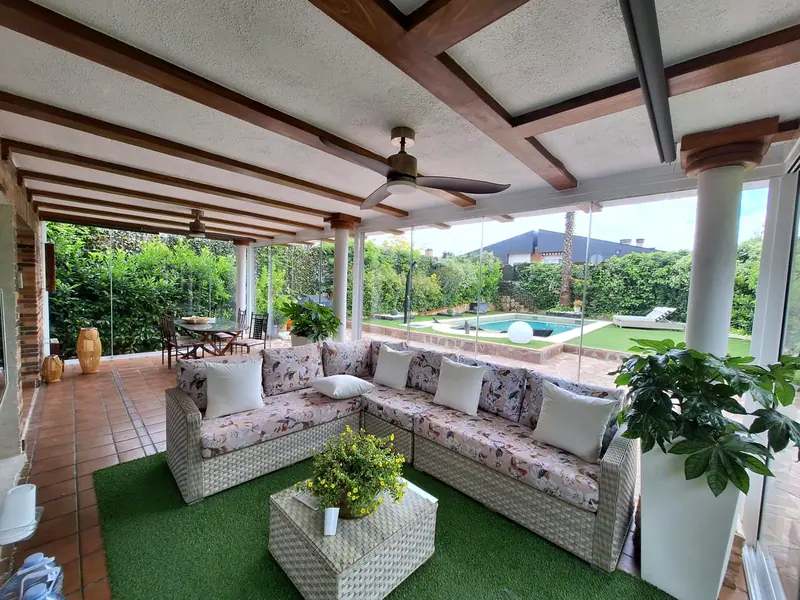 Porche rustico con cerramiento de cristal, zona de sofas y comedor con vistas a la piscina