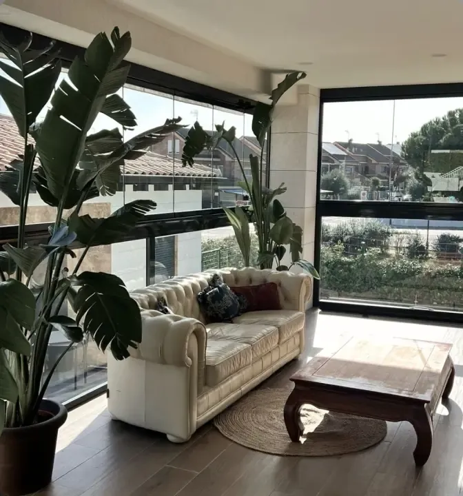 Salón con cortina de cristal que cierra la terraza en una vivienda de Madrid
