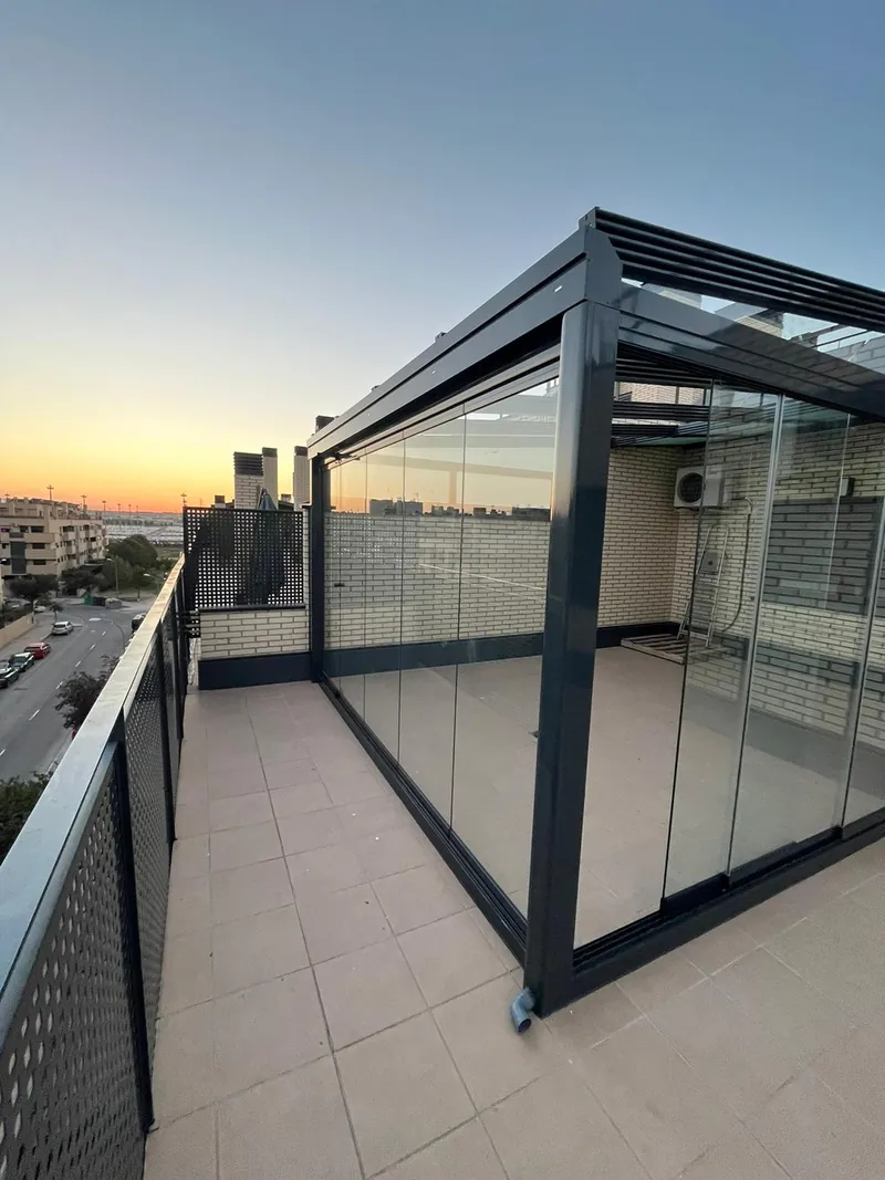 Cerramiento de cortinas de cristal en la terraza de un ático al atardecer