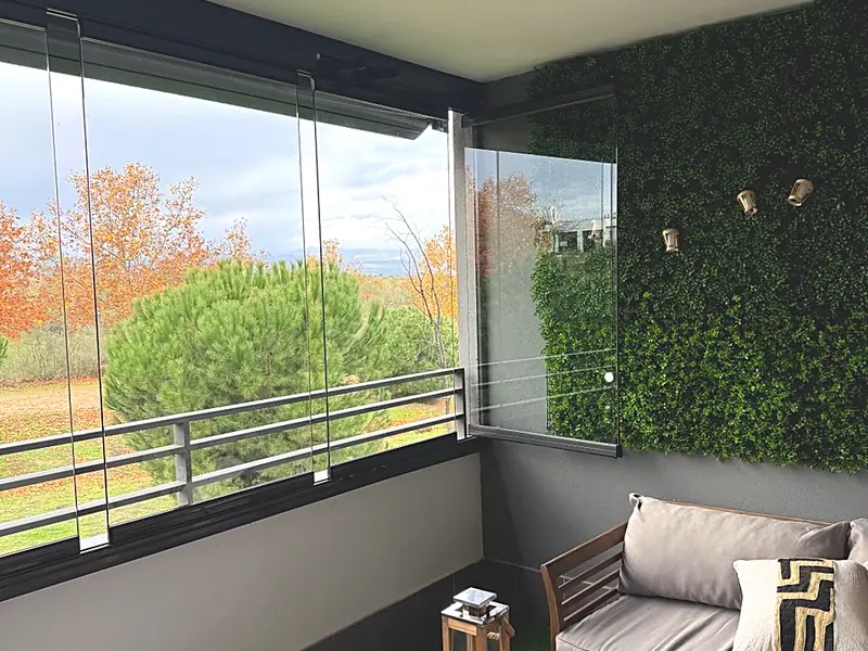 Terraza cerrada con cortinas de cristal, muro vegetal y sofá, con vistas al arbolado en otoño, en Madrid