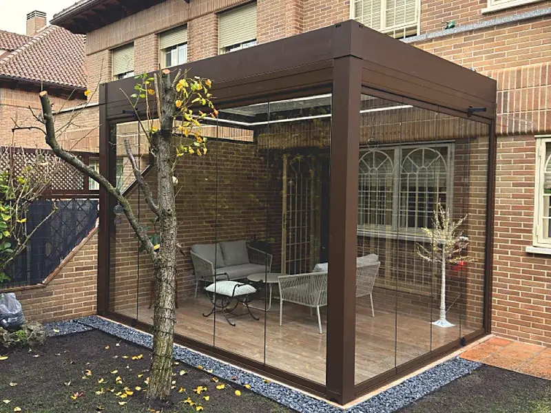 Pérgola bioclimática con los laterales cerrados con cristal en el jardín de una vivienda de Madrid