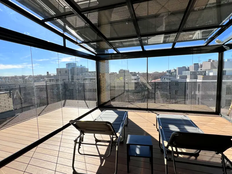 Techo de cristal móvil sobre la terraza de un ático de Madrid, con tumbonas y vistas a la ciudad