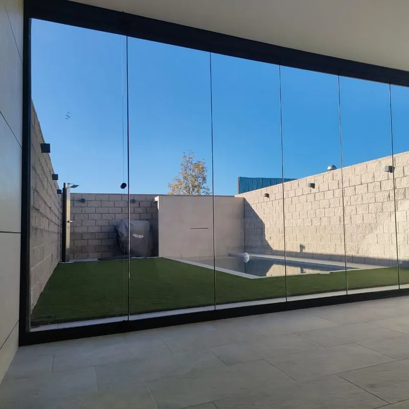 Patio con césped y piscina visto a través del cerramiento de cristal de una vivienda de Madrid