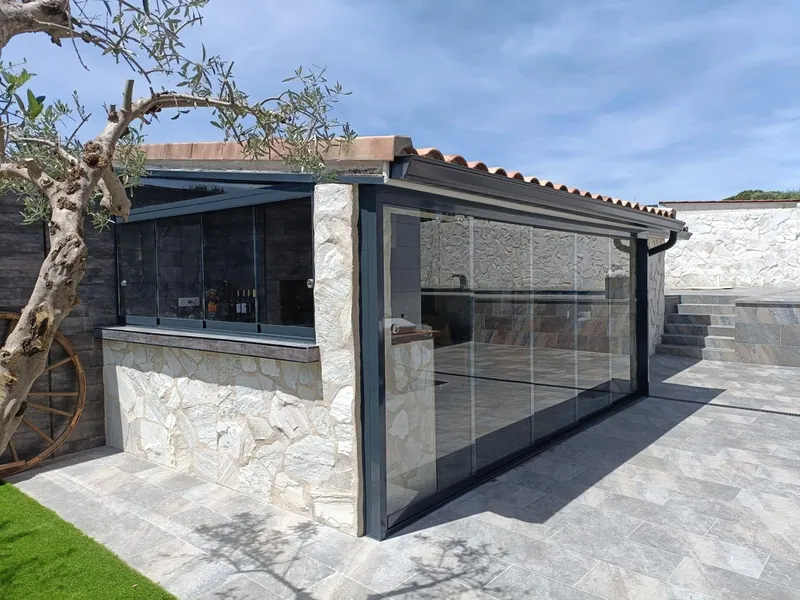 Cocina exterior cerrada con cristal junto a un olivo en una vivienda de Madrid