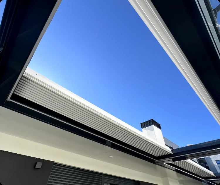 Pérgola bioclimática con las lamas retráctiles recogidas y el techo abierto del todo en una terraza de Madrid
