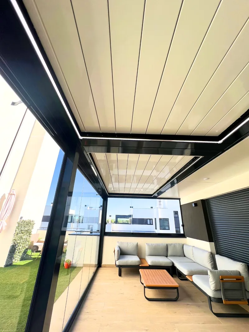 Pergola bioclimatica con iluminacion LED y cerramiento de cristal sobre zona de sofas en terraza