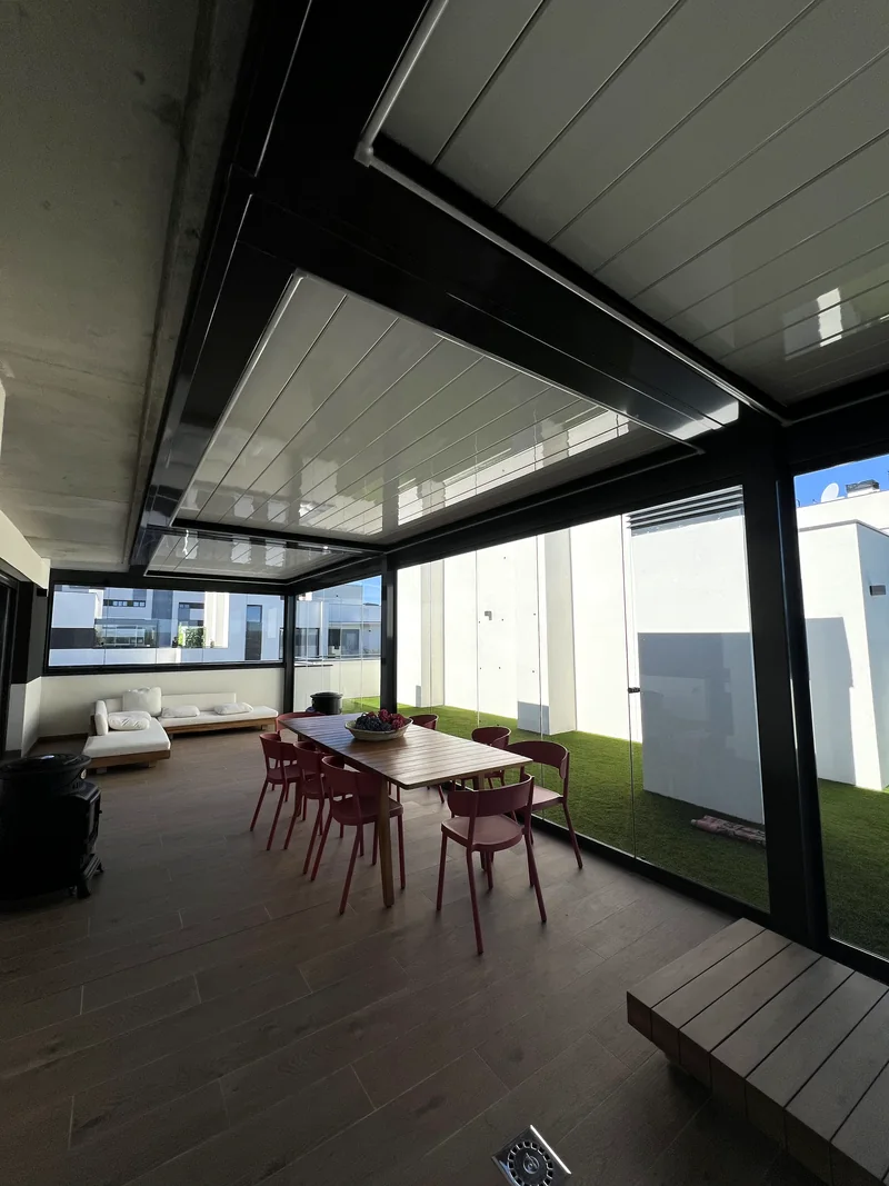 Terraza con pergola bioclimatica y cerramiento de cristal, mesa de comedor con centro de flores