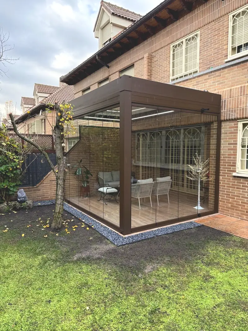 Pérgola bioclimática orientable cerrada con cristal en la esquina del jardín de una vivienda de Madrid