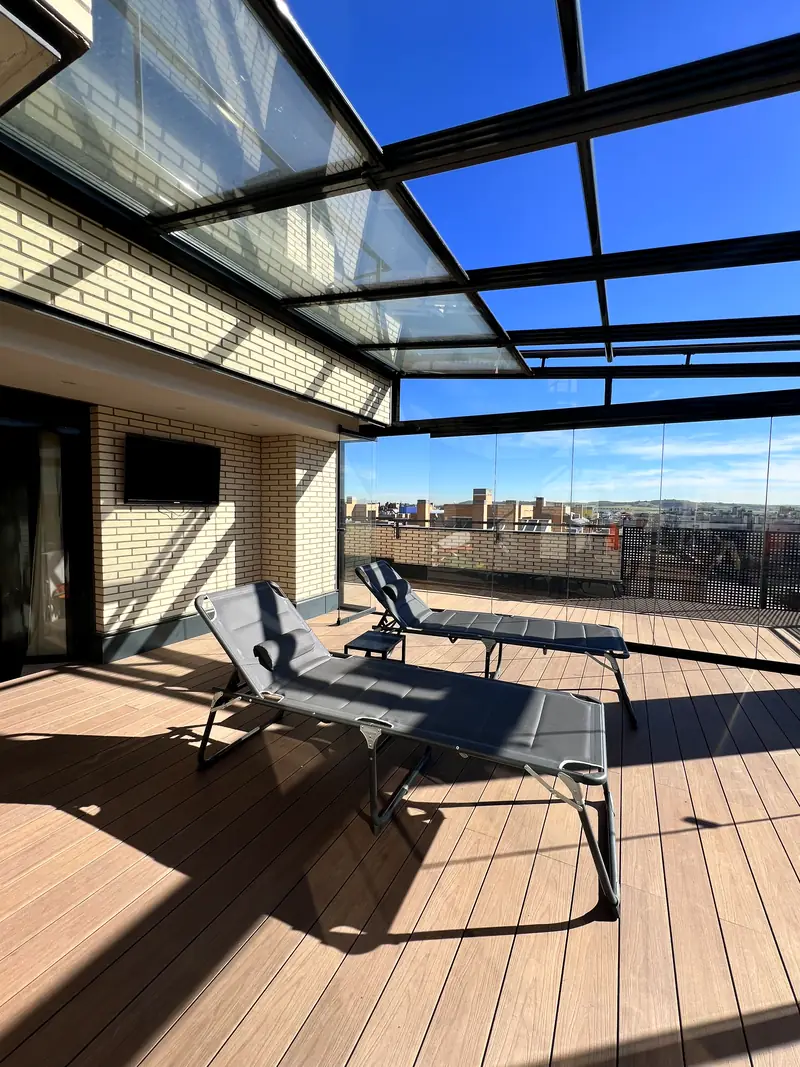 Techo de cristal fijo en terraza de atico con dos tumbonas y vistas a la ciudad